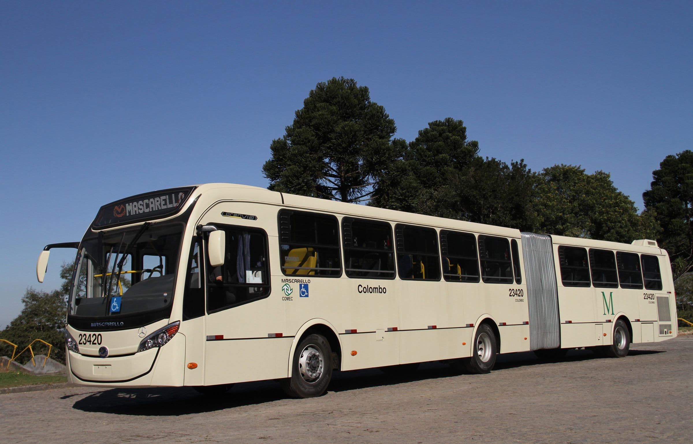 Ônibus articulado visto de frente, com árvores ao fundo