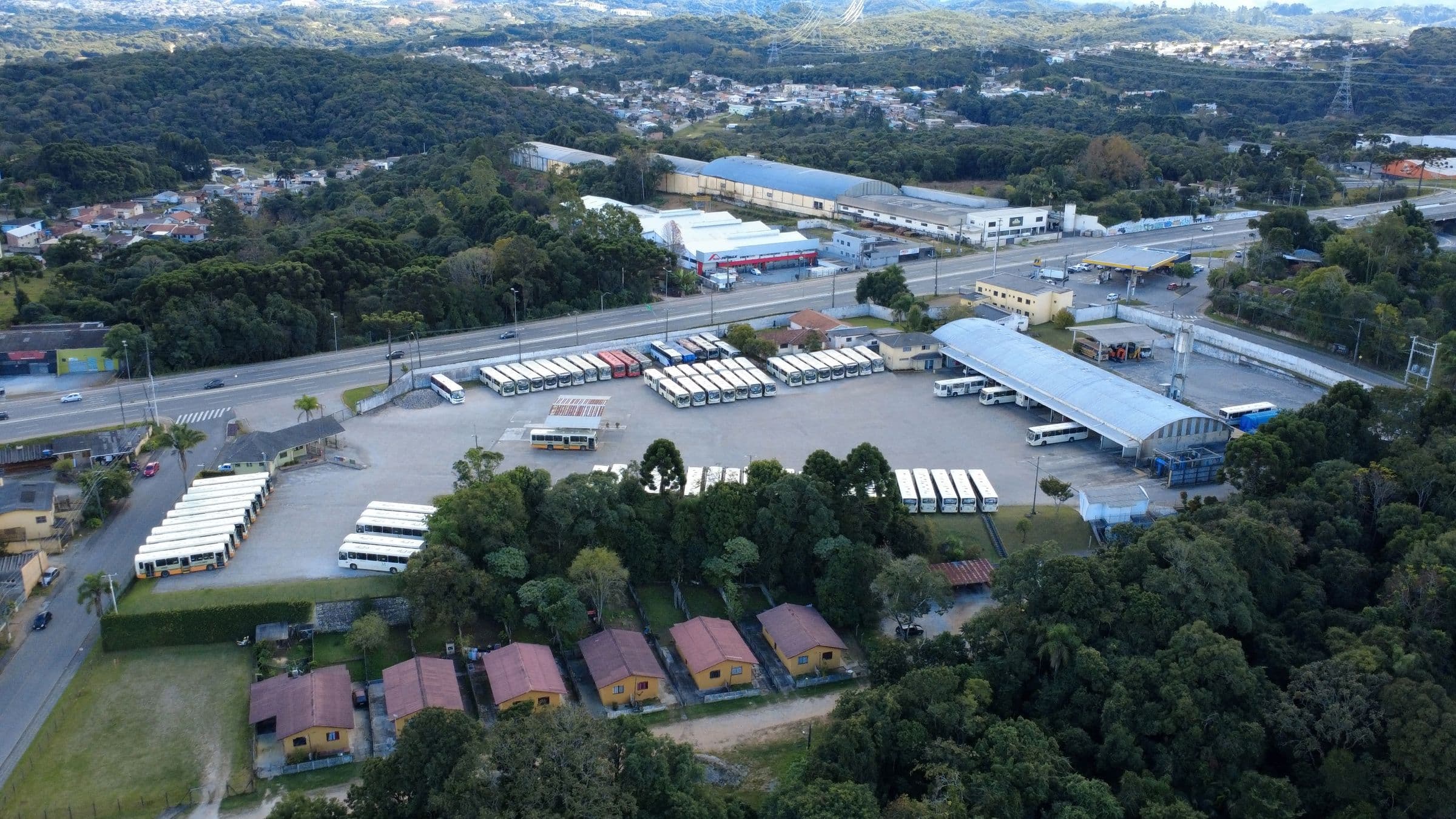 Vista aérea da garagem da Viação Colombo, com ônibus estacionados no pátio e mata ao redor